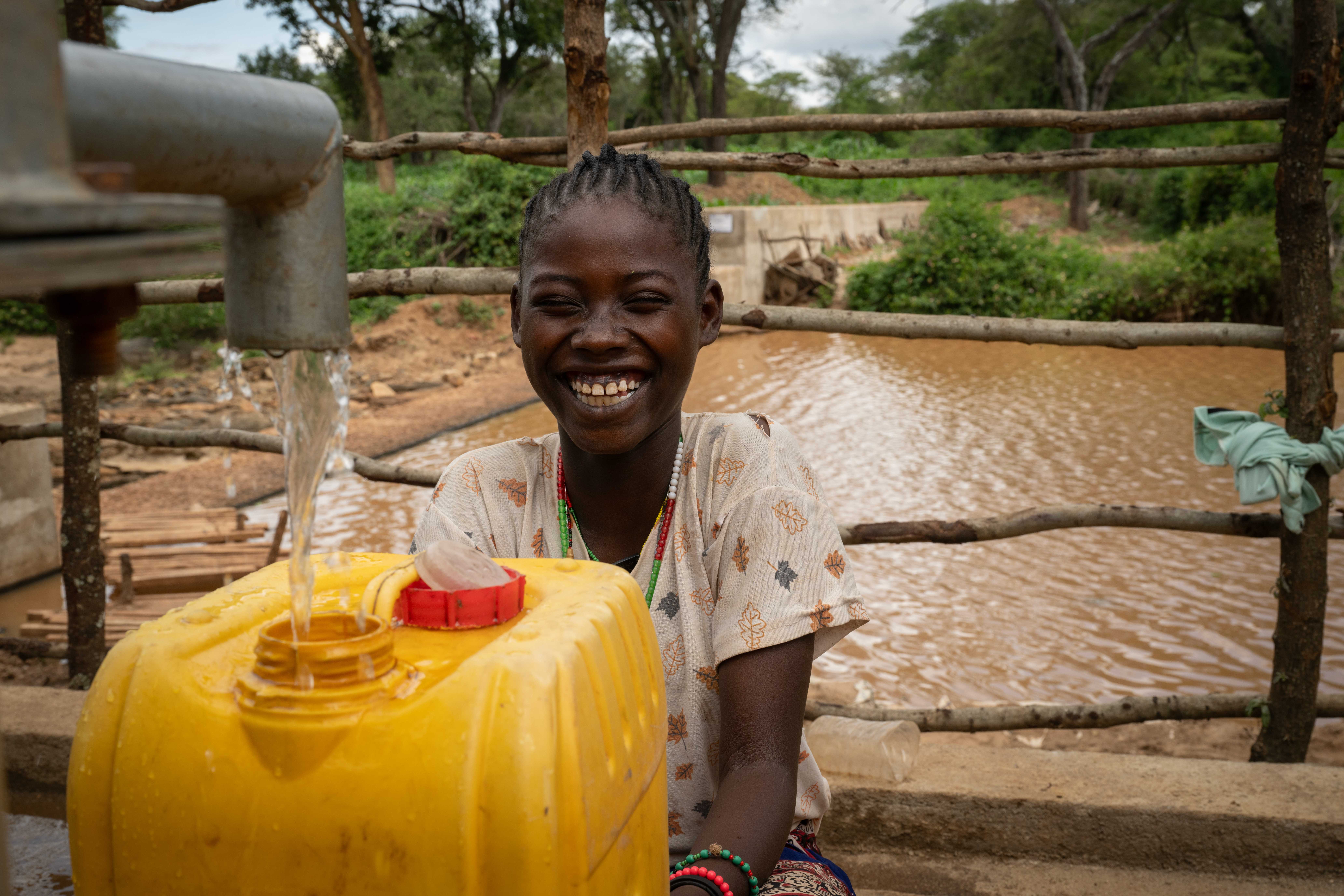 Bildet viser en ung jente i Afrika som fyller rent vann på en stor vannkanne.
